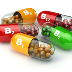 Kapsułki z witaminą B: B1, B2, B5, B6, B12. Każda kapsułka zawiera małe kuleczki z literą "B" i numerem witaminy.